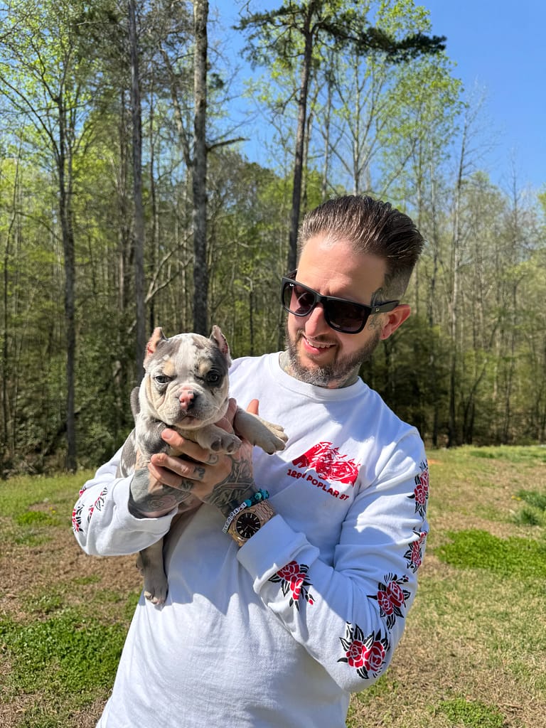 Matt holding Winnie, his tri merle micro bully puppy, on the day she went home from Southeast Bully Kennels, capturing the moment he received her as his birthday gift.
