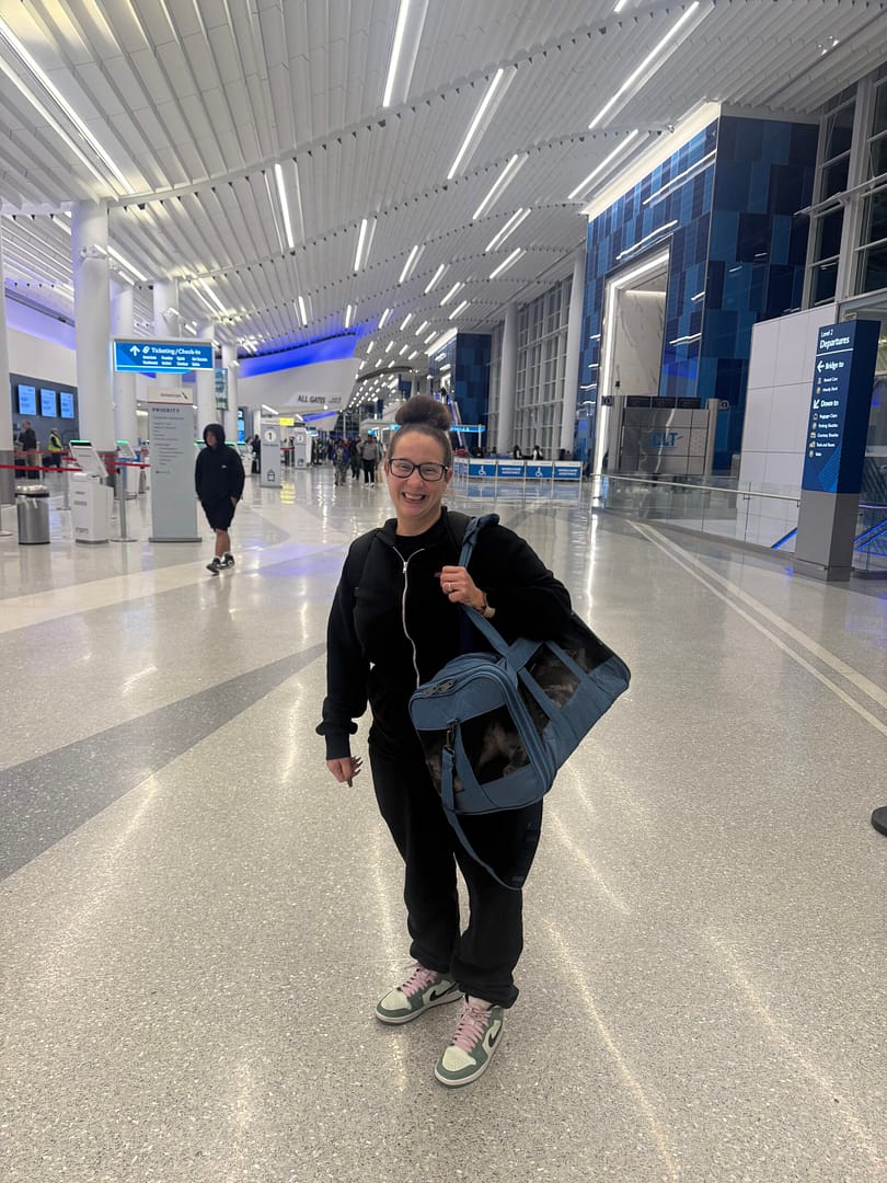 Veronica stands in the airport terminal holding a American bully puppy, preparing to pass through TSA as a pet nanny for Southeast Bully Kennels